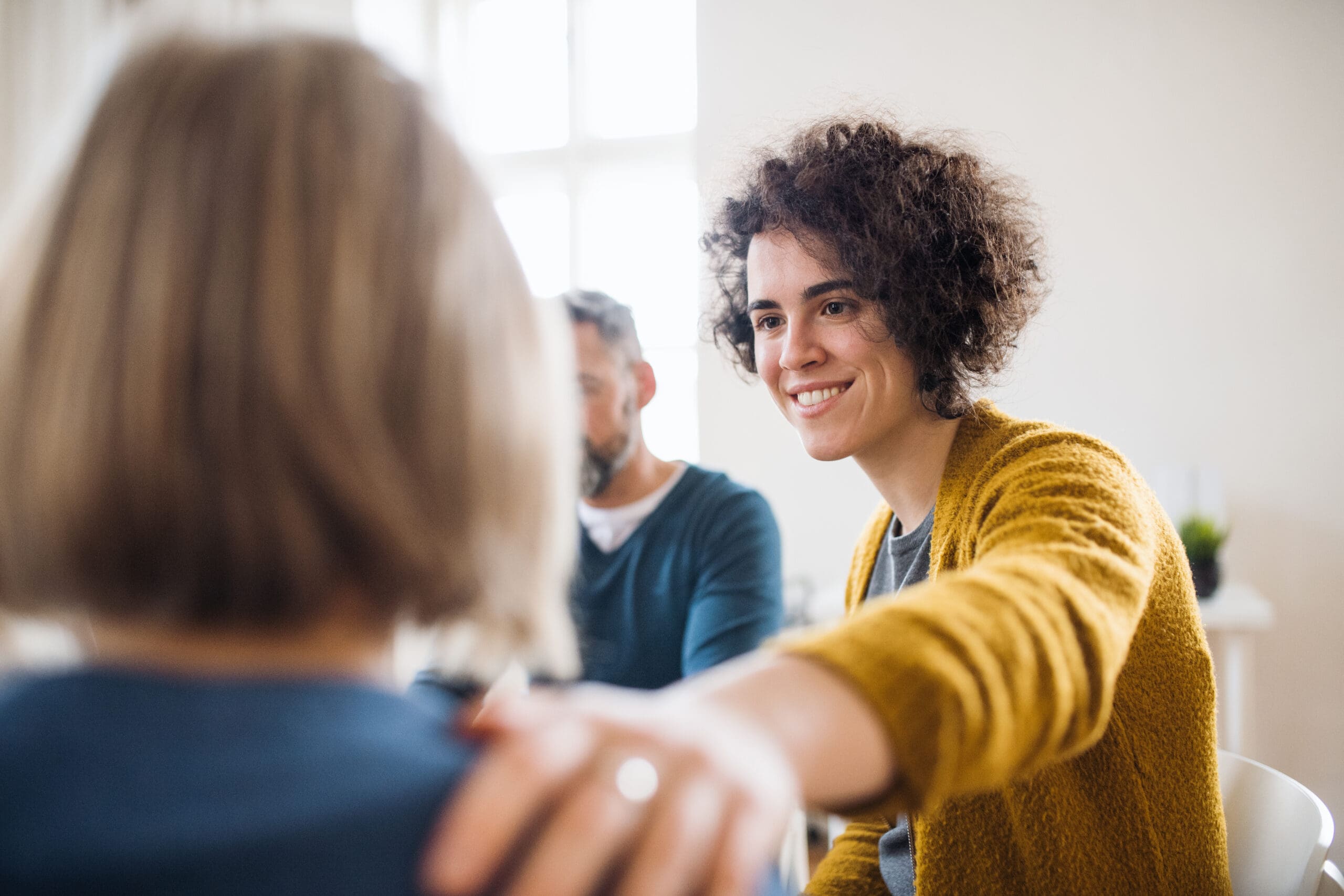 A woman places a supportive hand on someone's shoulder during a group therapy session