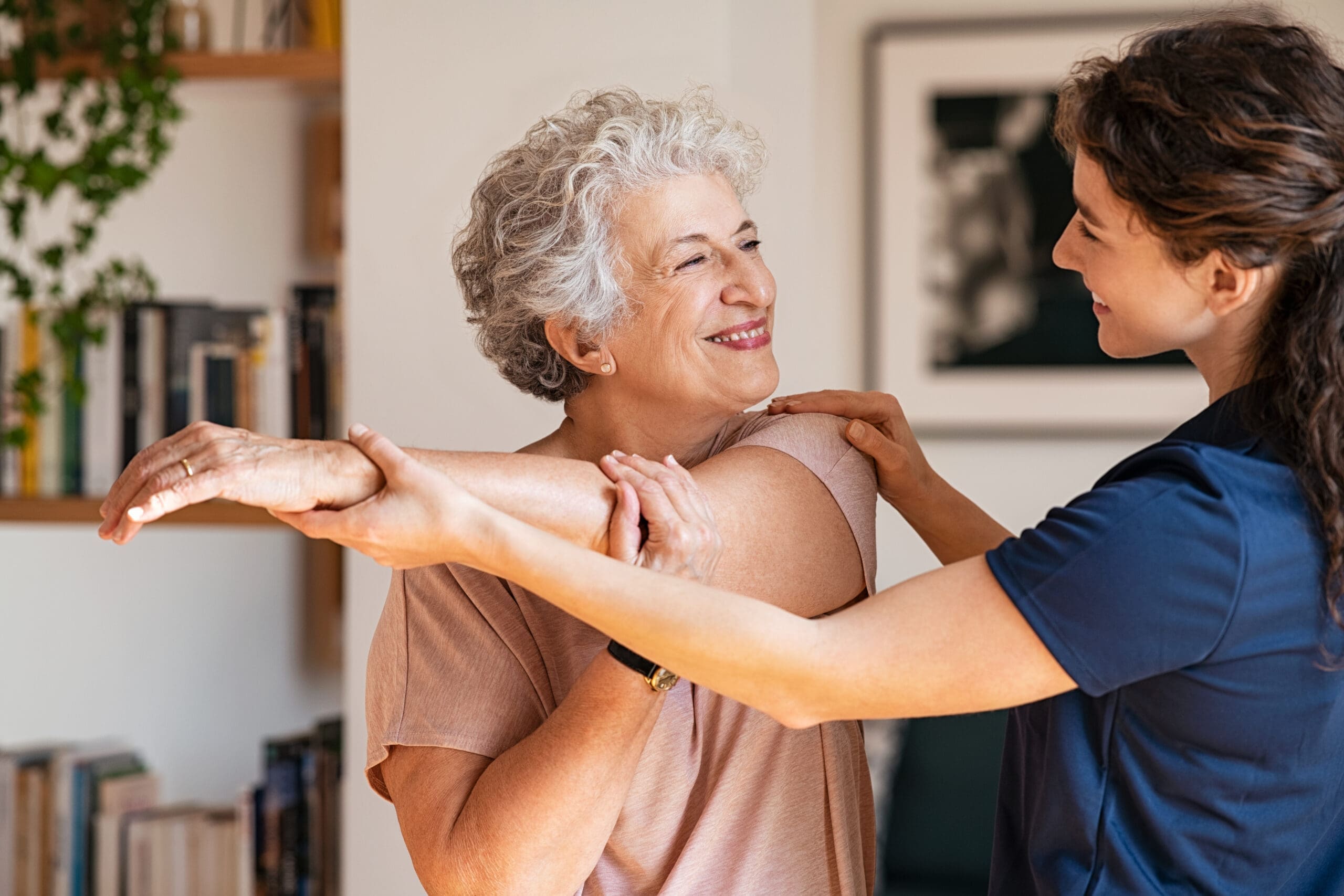 A carer helps an elderly woman do some stretches in her living room