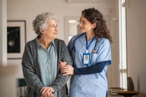 A young caregiver helps a senior woman walking down the hallway