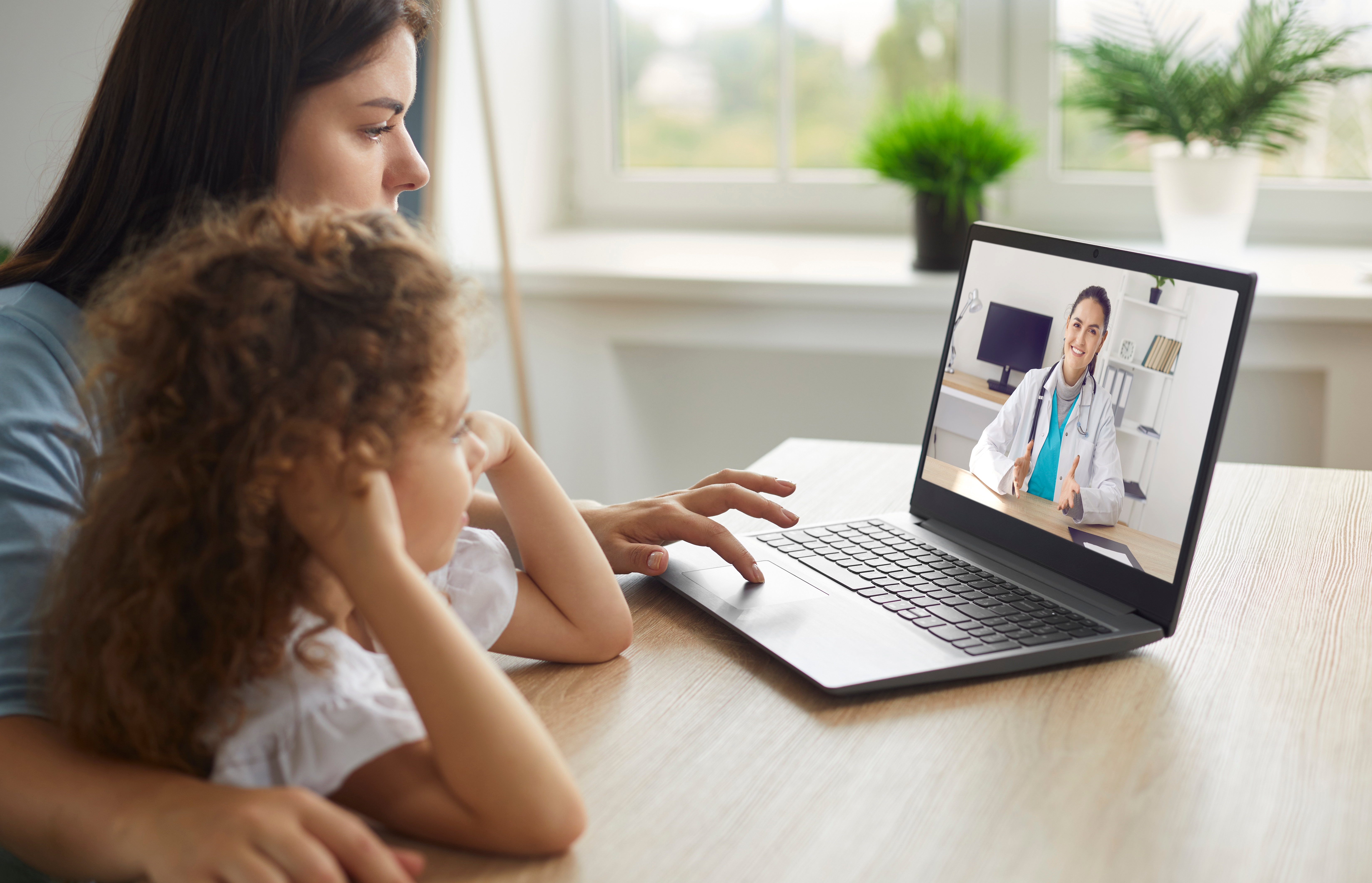 A mother and child watch a video of a doctor at a laptop