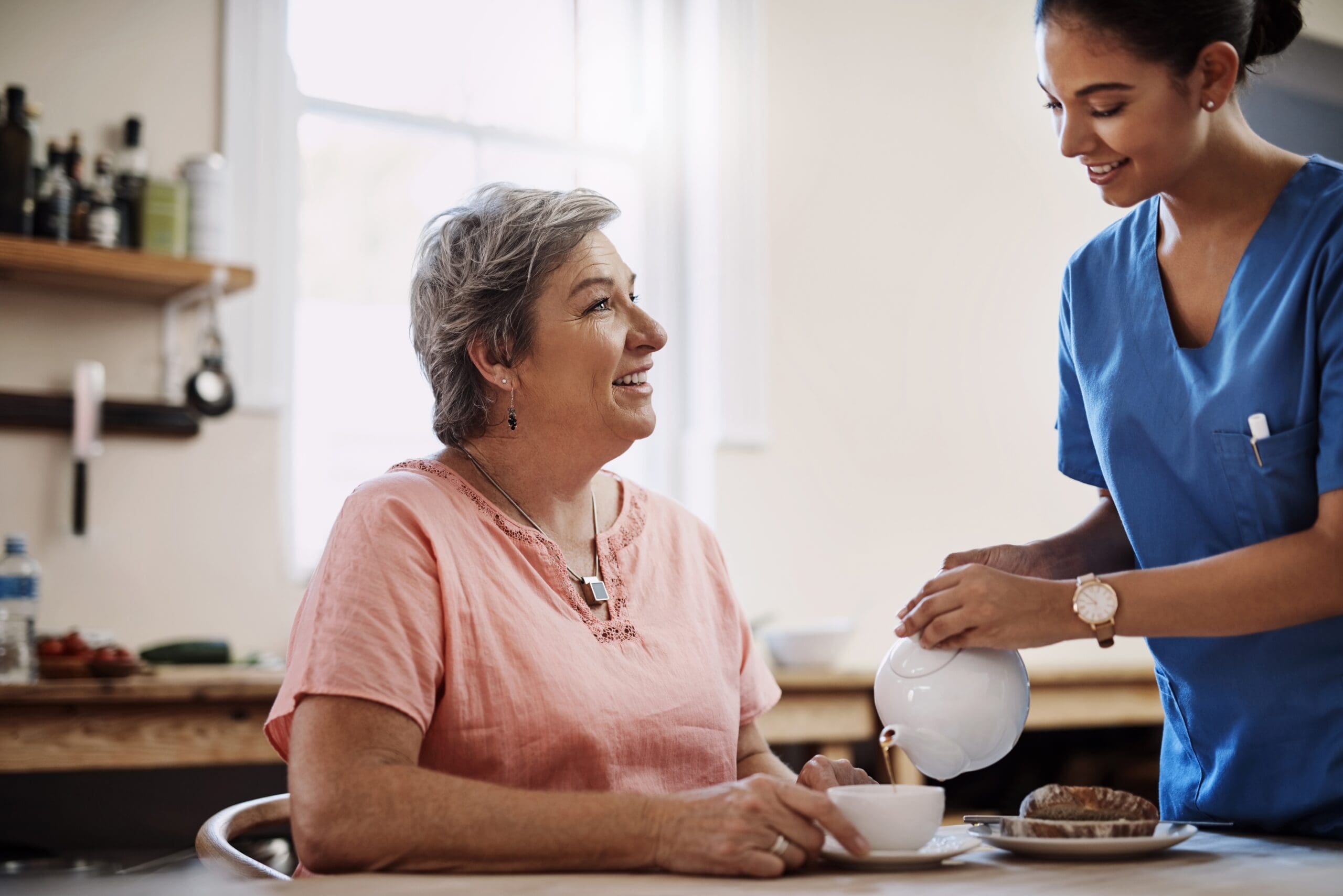 A woman and her carer share a pot of tea and a chat in the kitchen