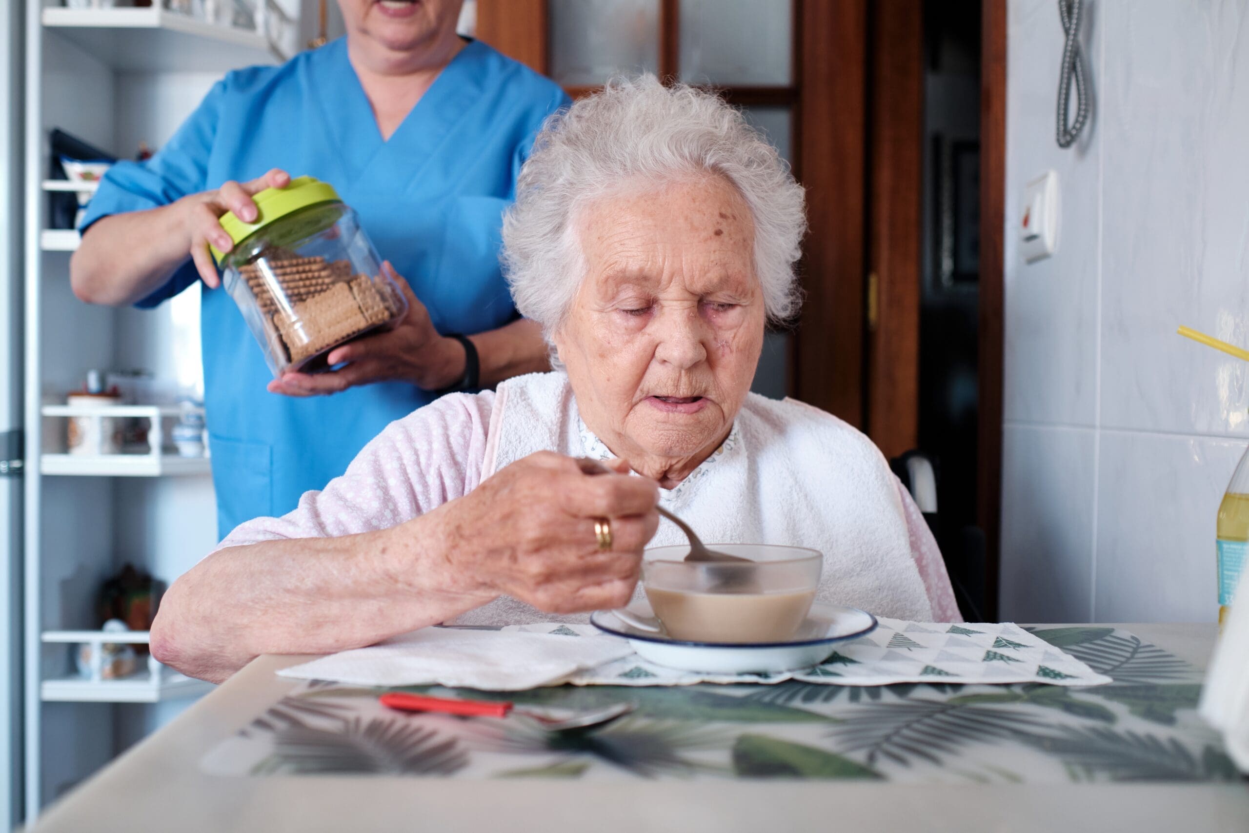 A carer gives an older woman a meal to feed herself
