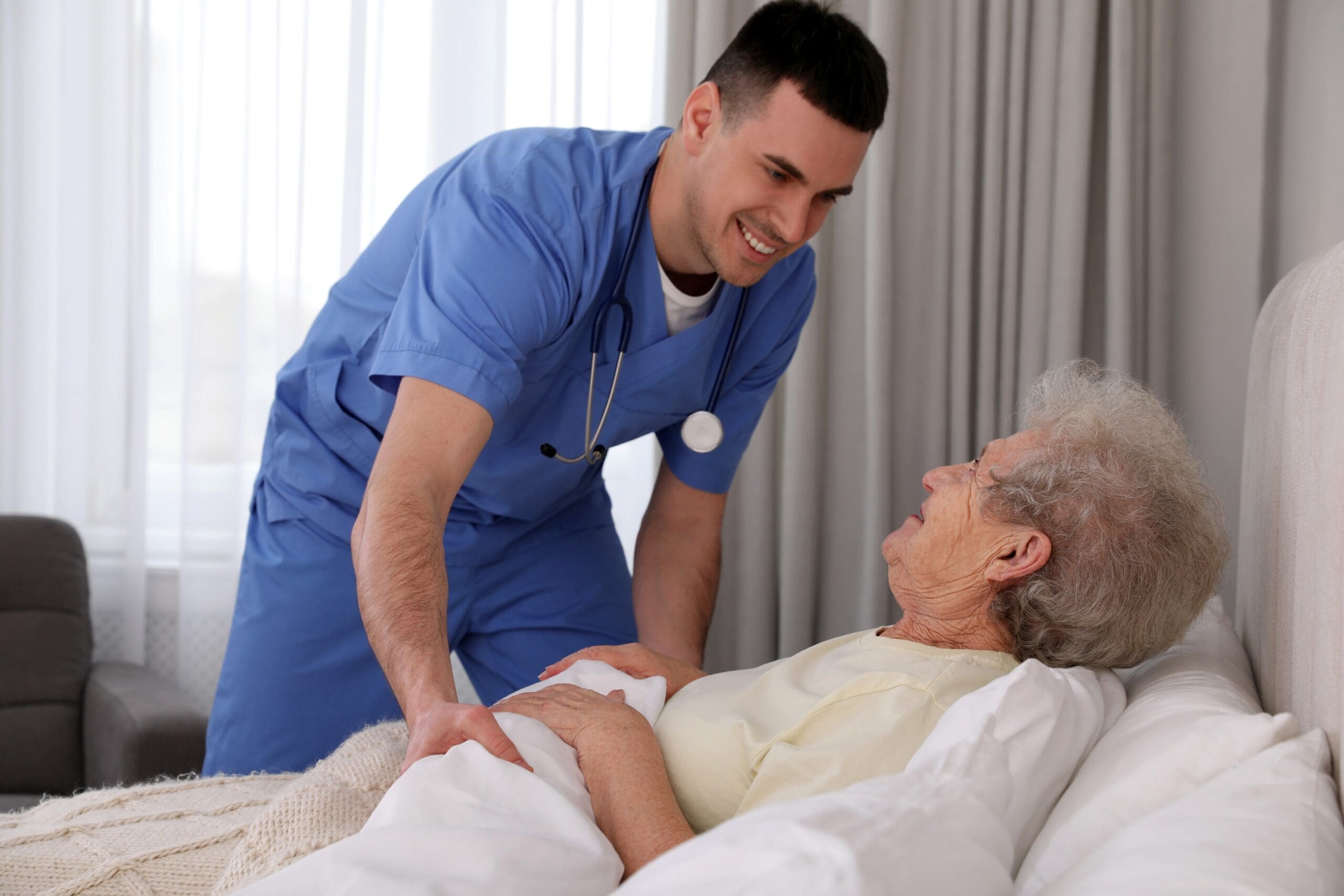 A care worker tucks an elderly woman into bed