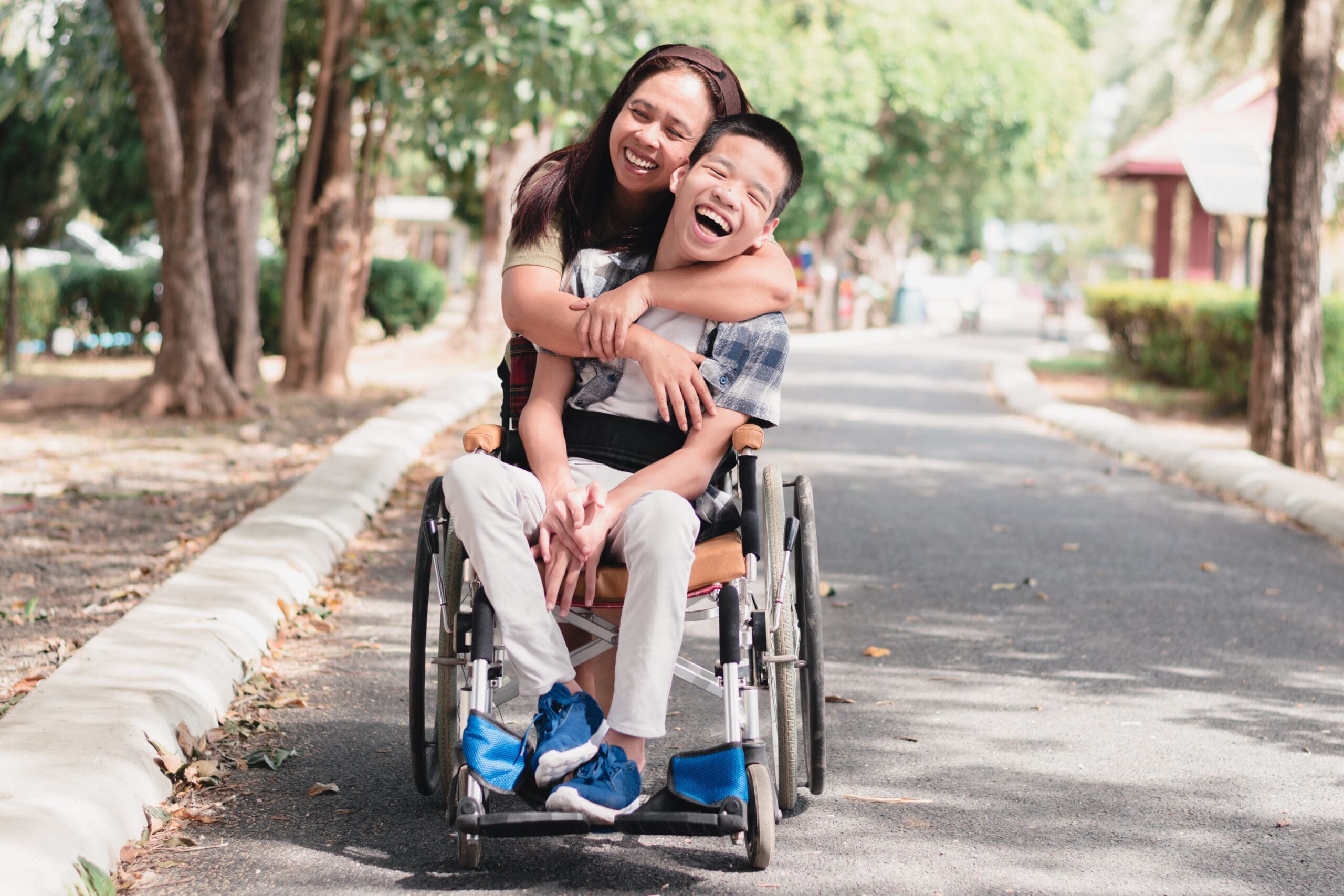 A woman hugs her disabled son from behind his wheelchair while he beams