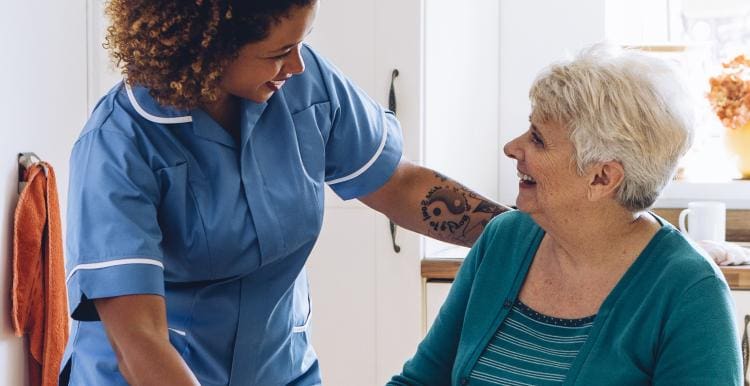 A carer and an older woman laugh together in her home