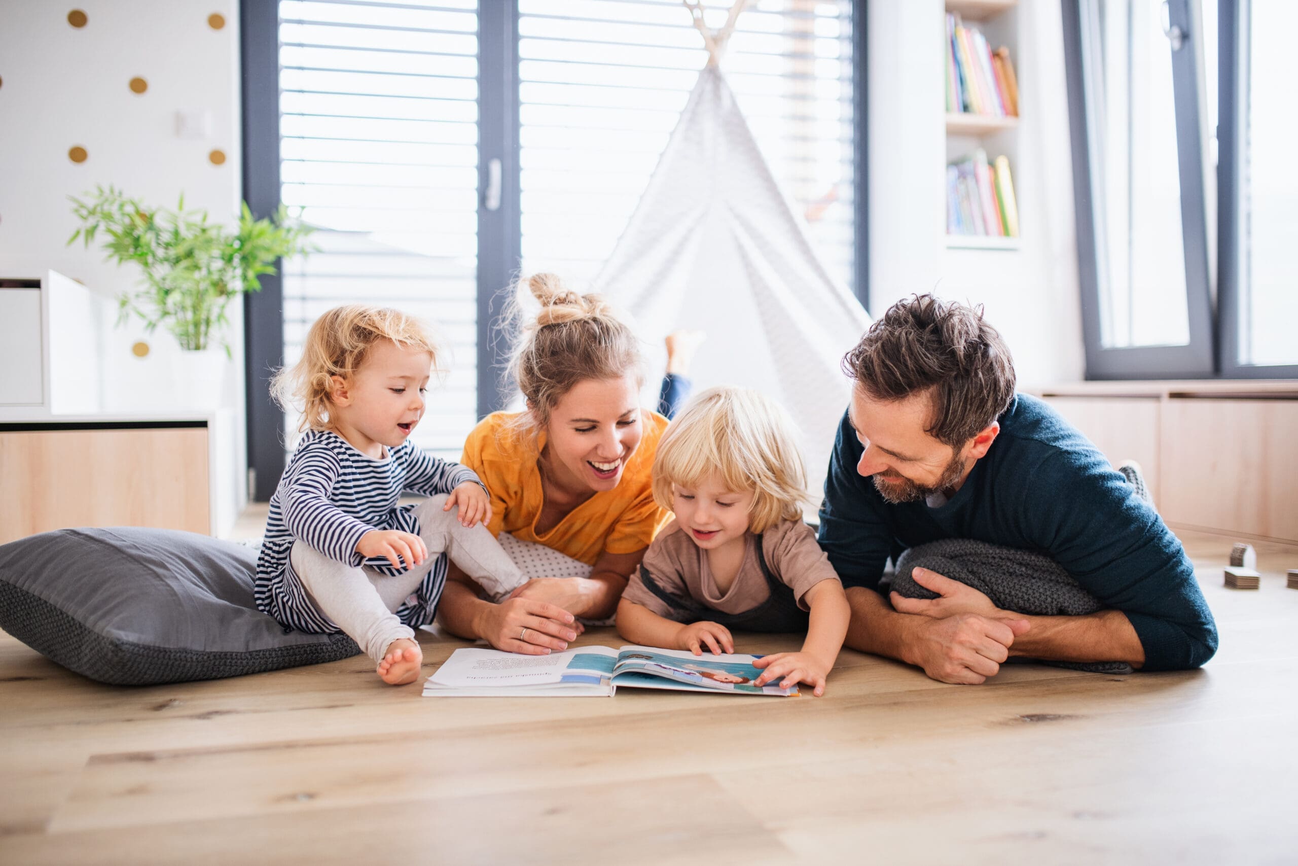 A happy couple lay on the floor in a makeshift tent with their smiling children