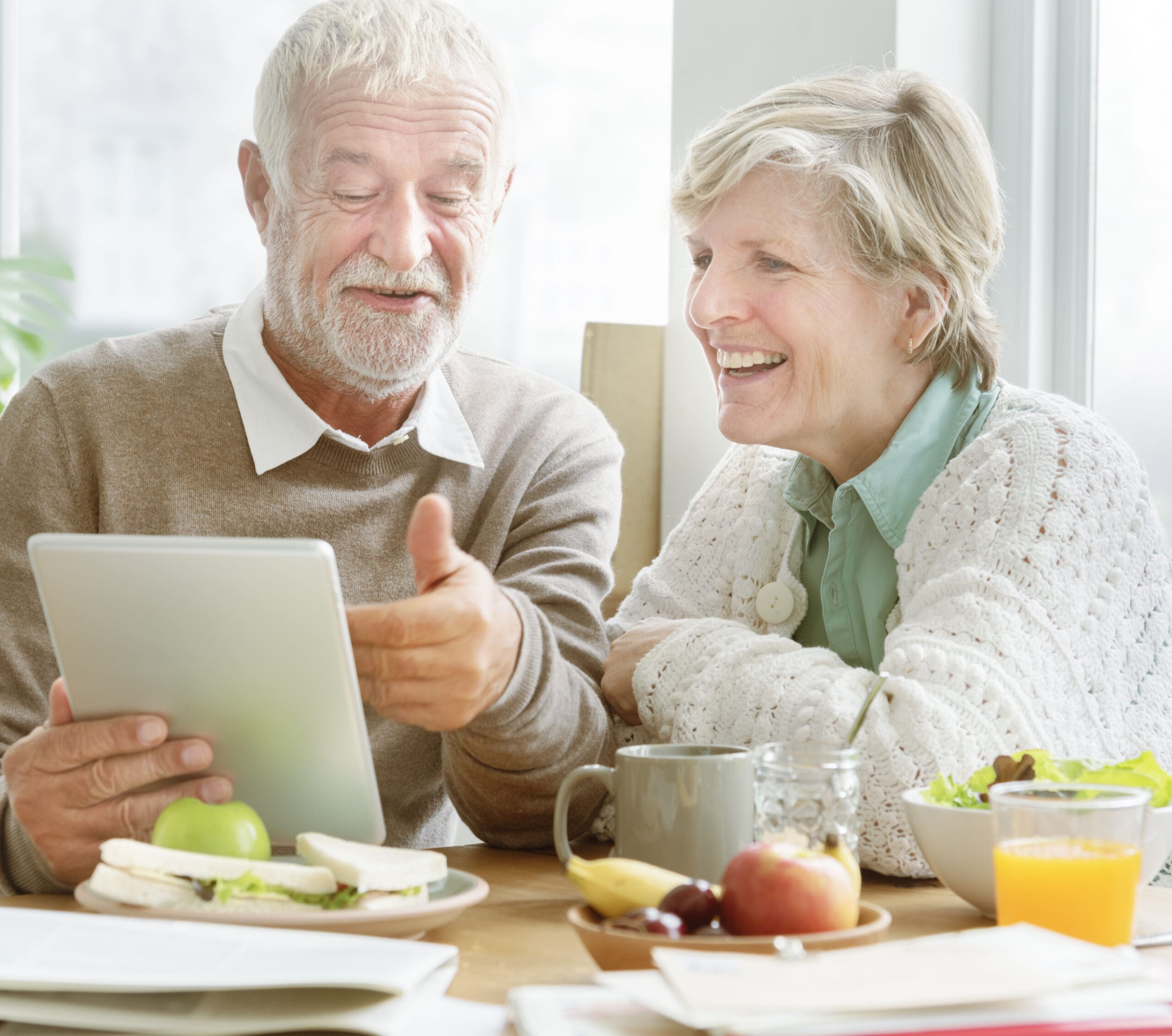 An older couple look at an ipad together over breakfast